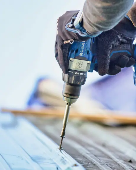 A gloved hand driving a drill into timber
