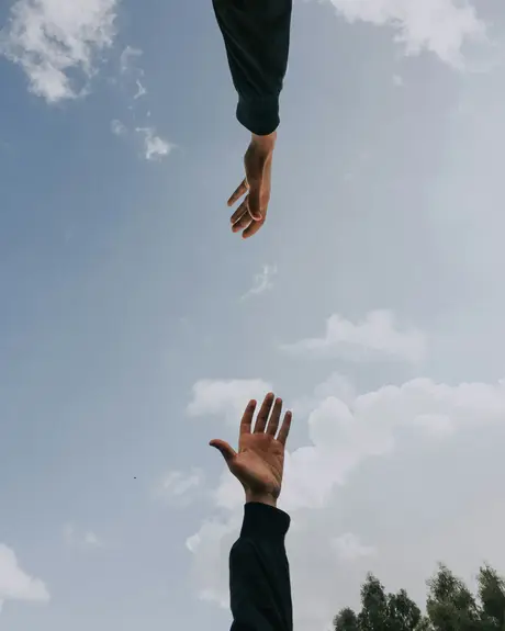 Two hands reaching toward each other against the sky