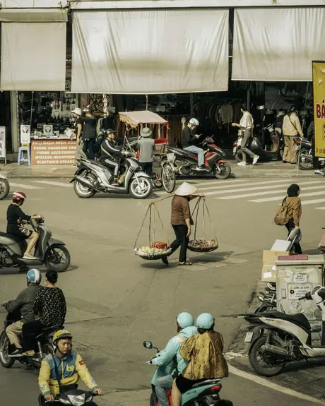 A street vendor carrying fruit baskets on a shoulder pole through Hanoi traffic