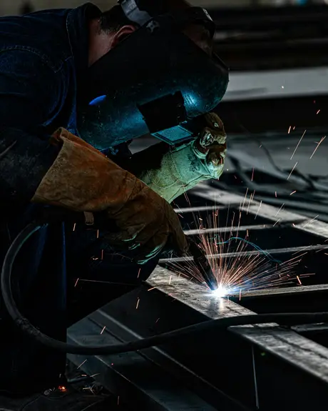 A welder in a mask, sparks flying off a steel beam